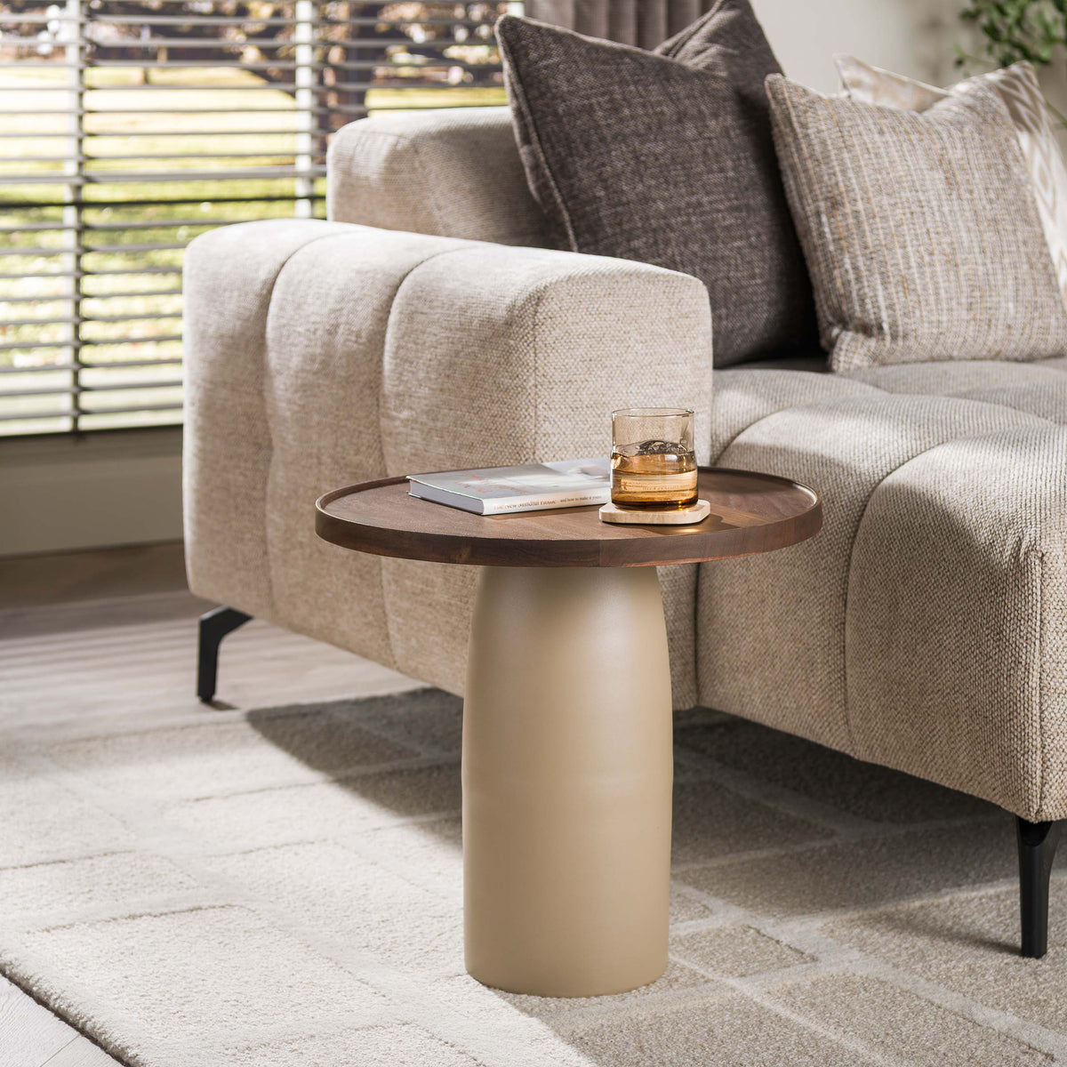 Bijzettafel Macy van Meubelista met bruin acaciahouten blad en beige voet, naast een lichte bank.
