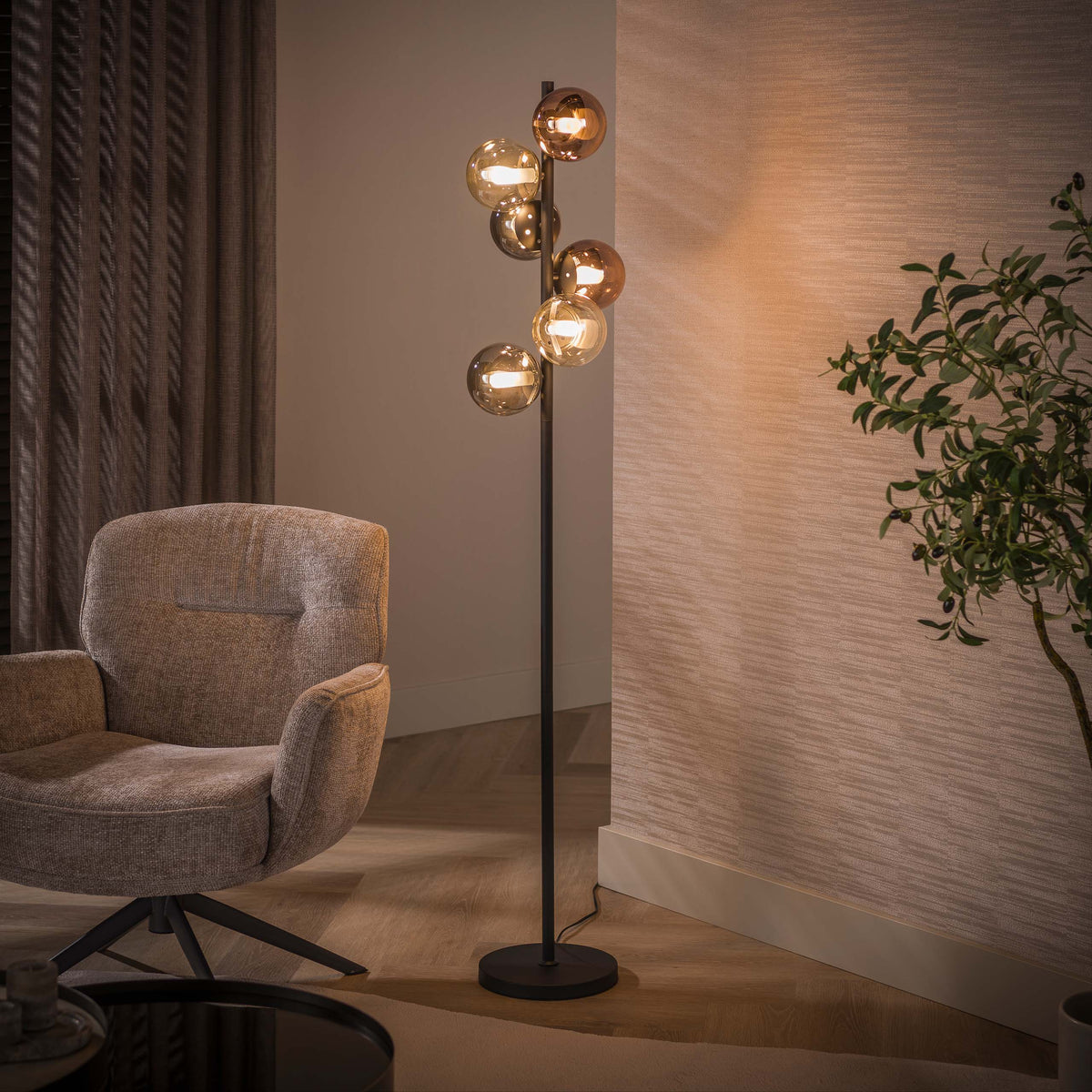 Vloerlamp Ovio van Meubelista in zwart: sfeerfoto met brandende glazen bollen naast een fauteuil.