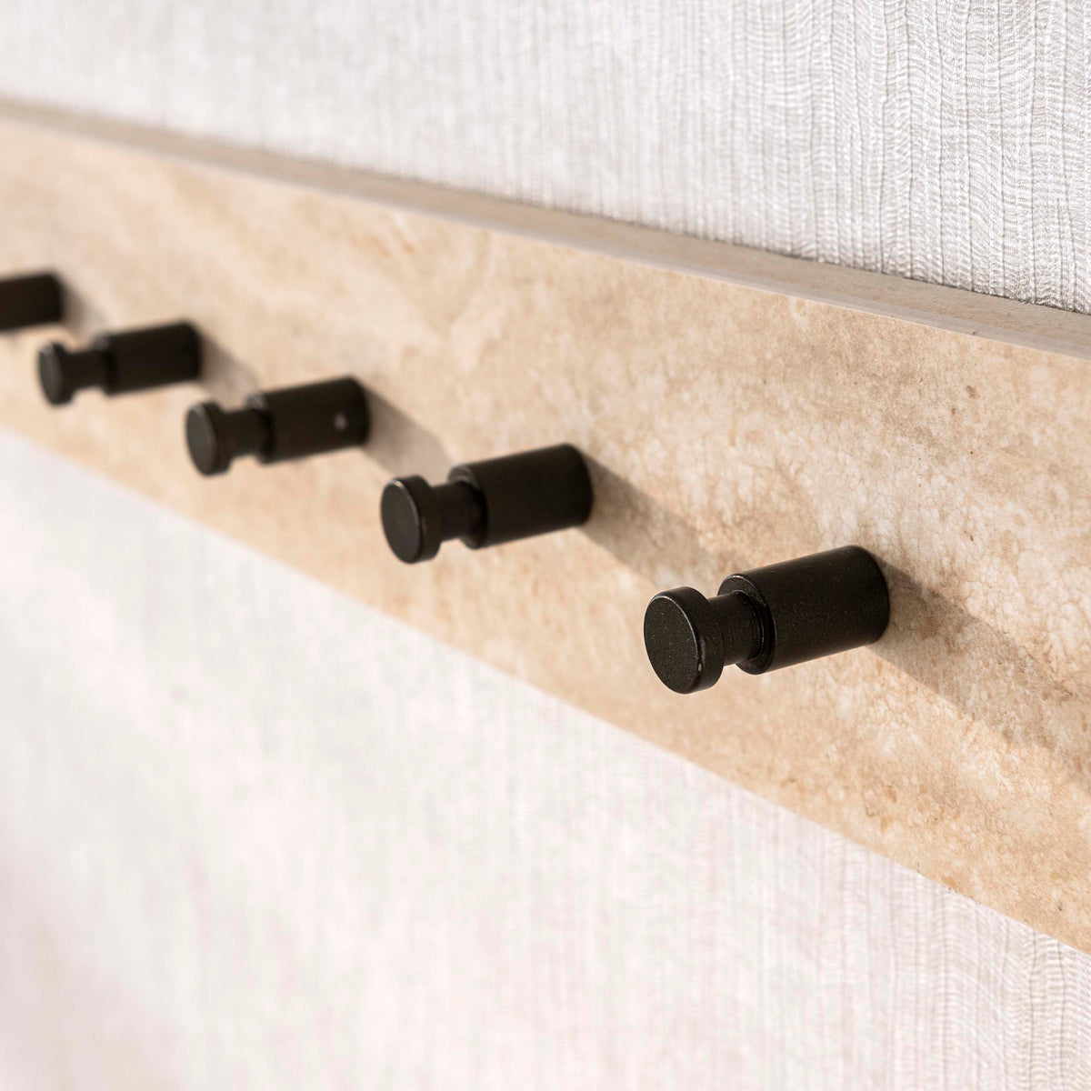 Kapstok Sava van Meubelista in beige: detail van de travertinlook en donkere haken.
